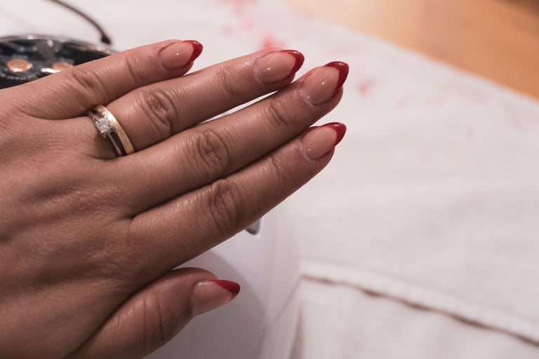 Sophisticated red French tip manicure on almond-shaped nails with gold wedding band and diamond ring