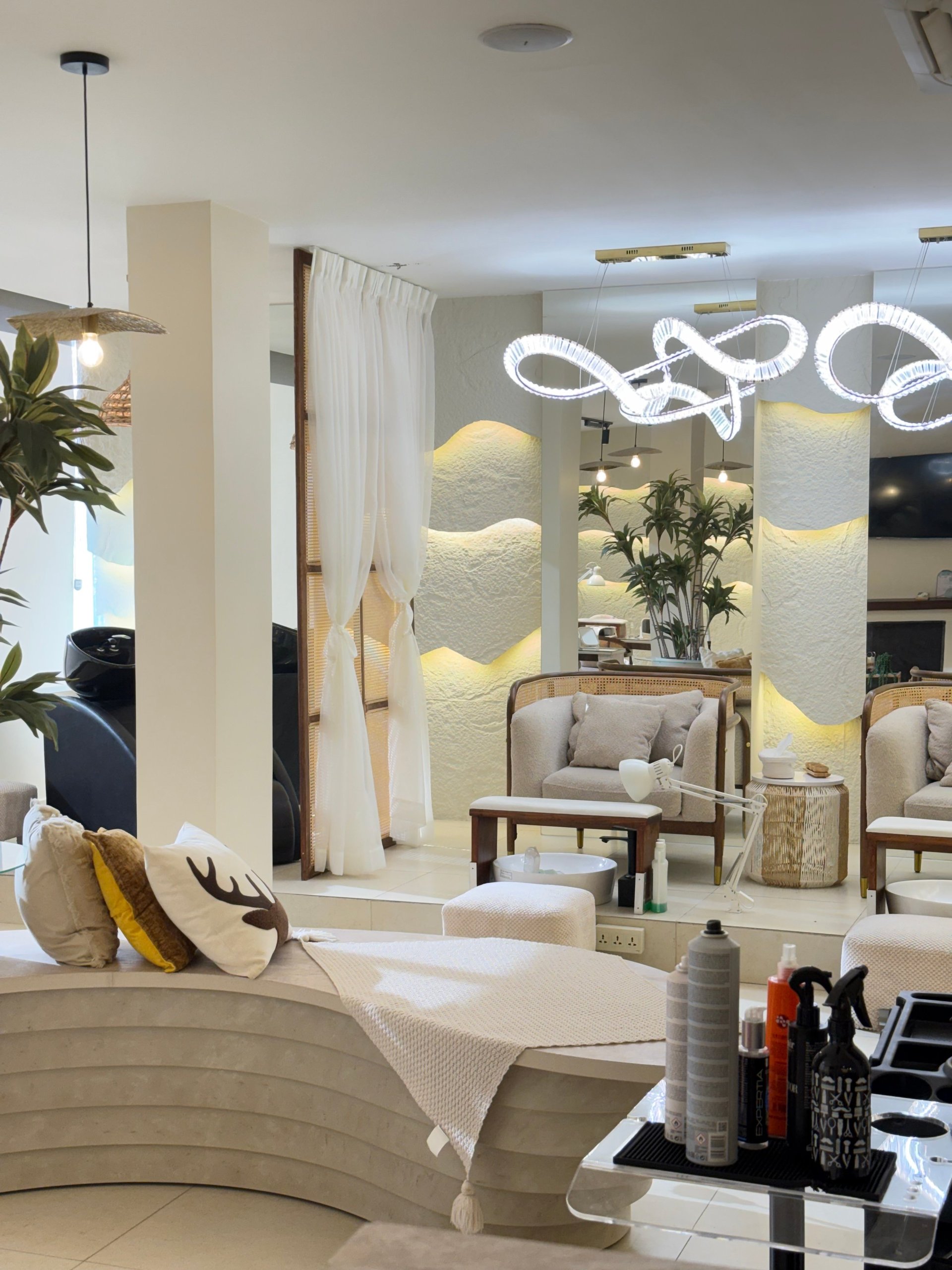 Modern beauty salon interior with curved white reception desk, neon signage, cream seating areas, textured wall panels, and ambient lighting