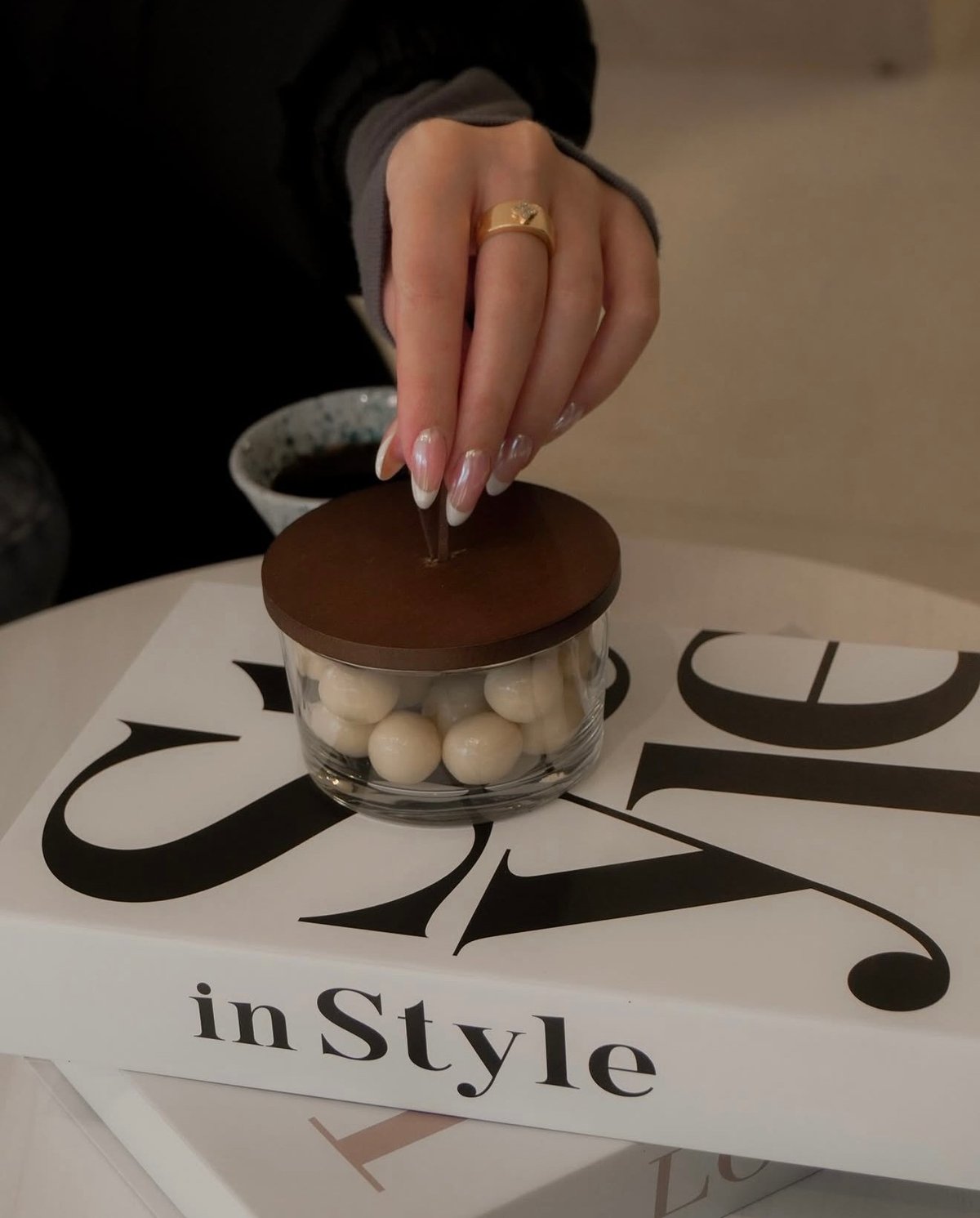 Manicured hand with gold ring placing lid on glass jar filled with pearls on inStyle magazine